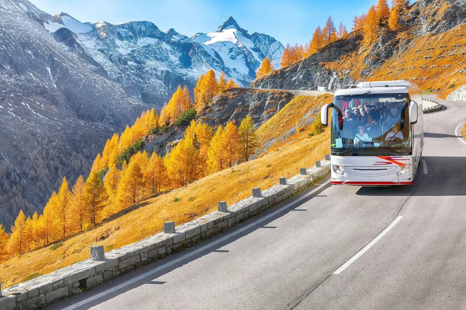 Blue coach driving along a mountain road with alpine peaks in the background