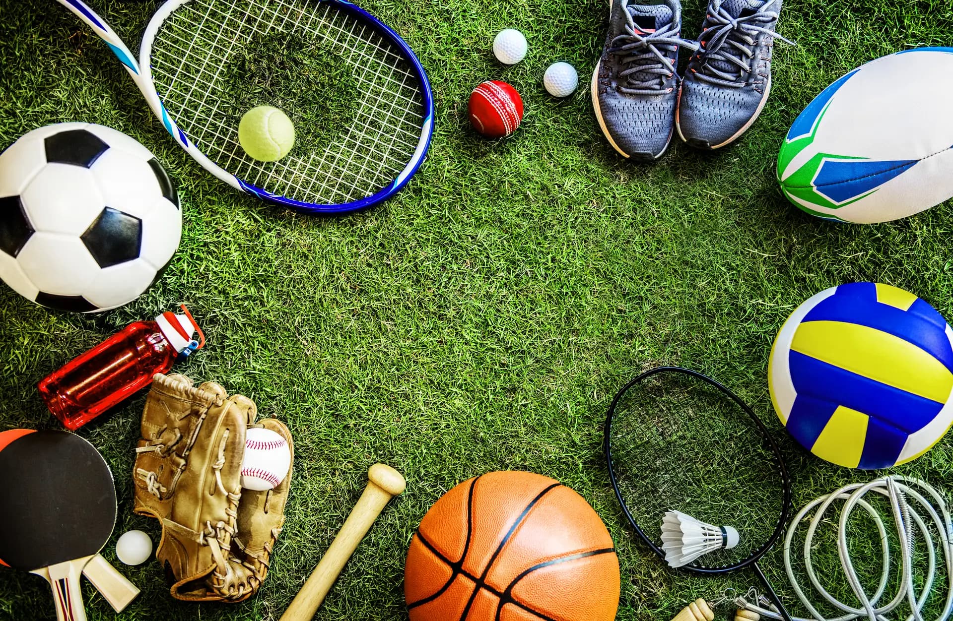 Různé sportovní náčiní na trávníku — fotbal, tenis, basketbal a další